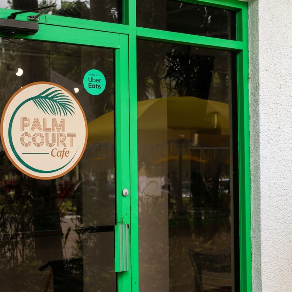 Green-framed glass entrance to Palm Court Cafe, featuring a round logo and Uber Eats delivery sticker.